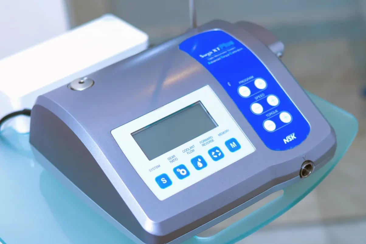 A close-up photograph of an NSK surgical micromotor console resting on a glass medical cart in a clinic.
