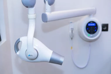 A photograph of a Dürr Dental intraoral X-ray machine with its articulated arm and wall-mounted control panel in a clinic.