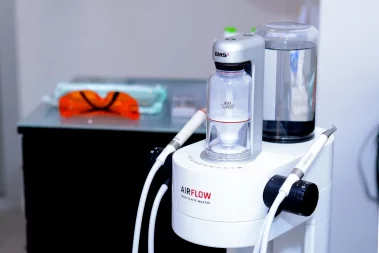 A close-up photograph of an EMS Airflow Prophylaxis Master dental cleaning unit with its powder chamber and hand pieces on a cart in a clinic.