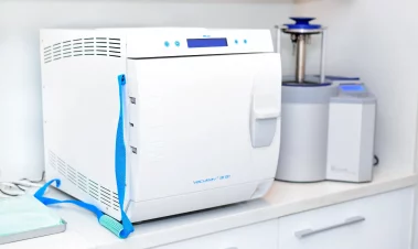 A close-up photograph of a MELAG Vacuklav sterilizer and other clinical sterilization equipment on a counter in a medical office.