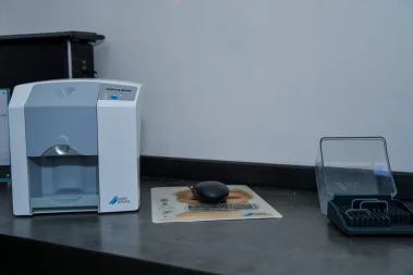 A close-up photograph of a Dürr Dental Vista Scan scanner, a computer mouse on a pad, and an imaging plate storage box on a counter in a clinic.