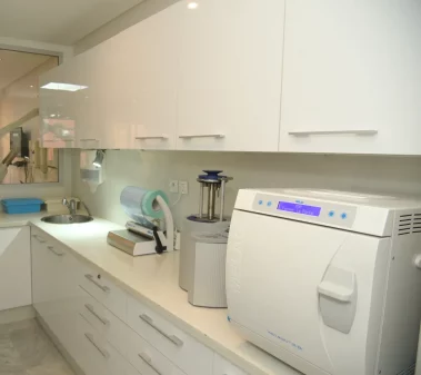 A photograph of a modern, sterile clinical preparation room featuring white cabinetry, a counter top sterilizer, a sealing machine, and a sink.
