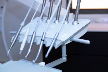 A close-up photograph of a dental delivery unit featuring multiple precision handpieces and hoses resting on their console in a clinic.