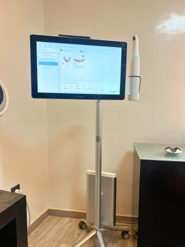 Mobile 3Shape digital scanning unit on a wheeled stand, displaying a patient's dental impression scans, with an intraoral scanner attached to the side.