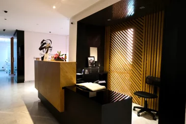 A modern dental clinic reception area featuring a wooden front desk, a black ergonomic chair, and a striking slat-wood accent wall with warm lighting.