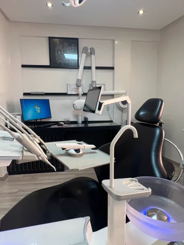 A modern dental treatment room featuring a black and white dental chair, an illuminated spittoon bowl, computerized equipment, and a framed typography wall art piece.